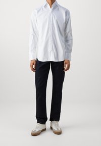 Witte overhemden met een spreidkraag, lange mouwen en een relaxte fit, gecombineerd met donkere jeans en witte sneakers met bruine accenten.