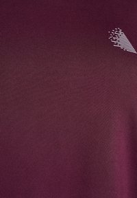 Bordeauxfarbenes Sportshirt aus einem glatten, strukturierten Stoff. Verfügt über eine kleine weiße Grafik auf der oberen rechten Seite. Sauberes, minimalistisches Design.