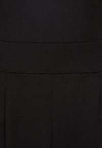 Tissu noir avec une texture lisse et un léger stretch. Doté d'une large taille et de plis pour un aspect sur mesure.