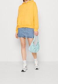 Gul huvtröja, denimkjol, ljusblå väska, vita strumpor och grå sneakers. Avslappnad outfit med mjuka texturer och färger.