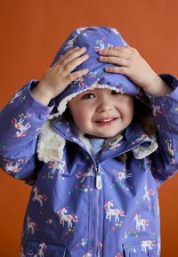 Lila wasserdichte Jacke mit einem Einhornmuster, blumigen Akzenten, weichem weißen Futter um die Kapuze und einem Reißverschluss.