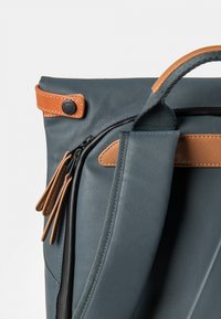 Donkerblauwe rugzak met tan lederen accenten, voorzien van een ritsvak, textuurstof en een handvat bovenop voor het dragen.