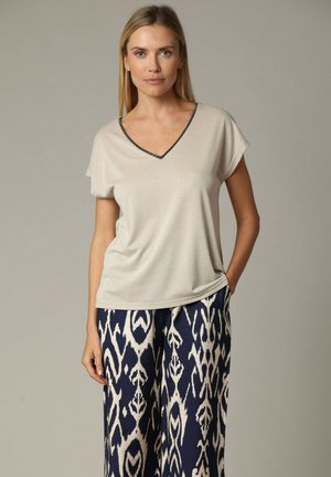 Beige korte mouw V-hals top van een textuurstof met zwarte biezen rond de halslijn, gecombineerd met marineblauwe patroon wijde broek.