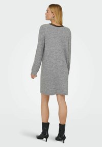 Vestido de punto gris con mangas largas y escote redondo. Presenta un borde de encaje negro en el cuello. Se lleva con botas negras hasta el tobillo.