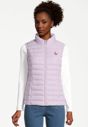 Veste sans manches en violet clair avec un col haut, fermeture éclair et coutures horizontales. Présente un petit logo sur la poitrine. Portée par-dessus un haut à manches longues blanc.