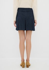 Denim A-linje kjol i mörkblått med vertikala ränder, med veck vid fållen. Buren med en ljusfärgad långärmad topp.