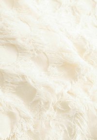 Witte textuurstof met rafelige randen en verhoogde cirkelvormige patronen gelijkmatig verspreid over het oppervlak. Zacht materiaal met een lichte glans.