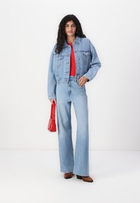 Ljusblå denimjacka, röd topp och ljusblå jeans med hög midja. Håller en liten röd handväska. Svarta klackstövlar.