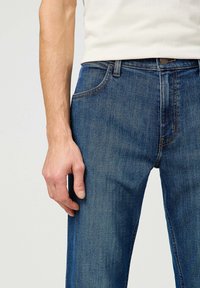 Vaqueros de mezclilla azul con un diseño de pierna recta, que cuentan con una disposición clásica de cinco bolsillos y costuras en contraste.