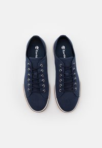 Baskets en toile marine avec semelles en caoutchouc blanc, dotées de six œillets métalliques et d'un design à lacets traditionnel. Logo de la marque visible à l'intérieur.