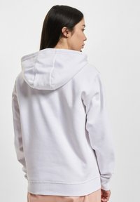 Hvit hettegenser med myk tekstur, elastiske mansjetter og avslappet passform. Har en stor hette og en lett senket skulderdesign.