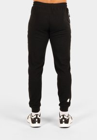 Zwarte sweatpants met een geribbelde textuur, elastische tailleband en zijzakken. Opvallend wit logo op het onderbeen. Gecombineerd met witte sneakers.