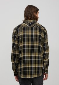 Camicia in flanella a quadri nera, verde e gialla con maniche lunghe, polsini con bottoni e dettaglio sulla schiena, caratterizzata da una vestibilità rilassata.