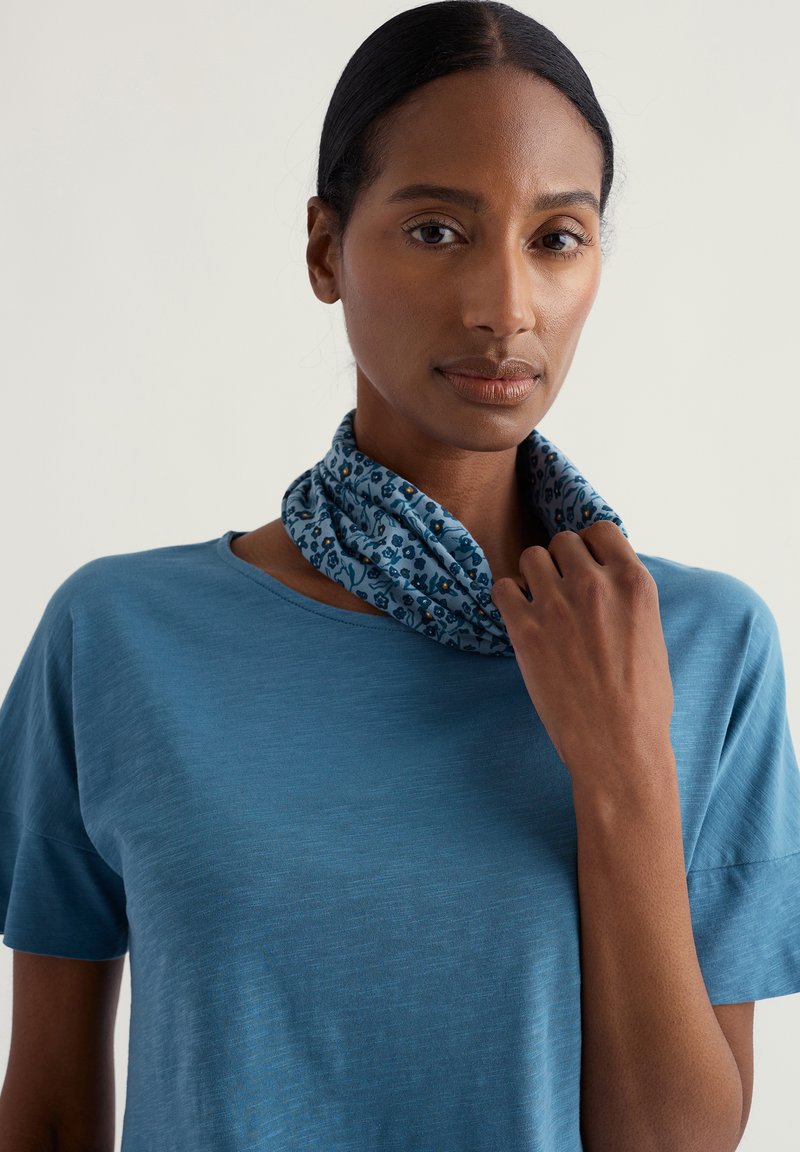 Sinine kerge lühikeste varrukatega T-särk, mida täiendab sinine kaelussall väikeste lillediga mustriga. Sile tekstuur.