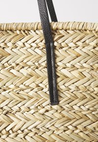 Geflochtene Strohtasche in natürlicher Farbe mit schwarzen Ledergriffen und einer strukturierten Oberfläche im Kreuzmuster.