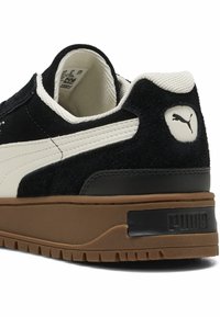 Crne suede i kožne tenisice s bijelom prugom, gumeni potplat i naglasak s logom na peti. Tekstuirana gornja strana dodaje detalj.