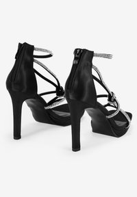 Sandalias negras de tacón alto con un acabado de cuero suave, diseño con tiras, cierre de cremallera en la parte trasera y acentos decorativos de strass.