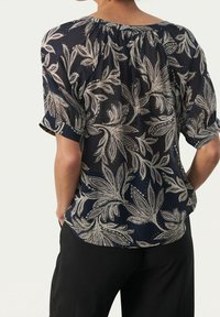 Blusa navy con un motivo floreale in crema, caratterizzata da un colletto arricciato e maniche corte, tessuto semitrasparente e vestibilità ampia.