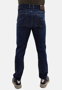 Jeans in denim blu scuro con taglio dritto, dotati di tasche posteriori curve e un'etichetta in pelle marrone sulla vita.