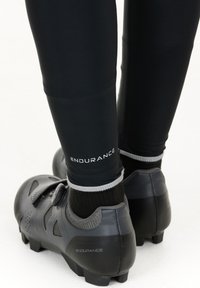 Black cycling shoes with a textured leather exterior, grey accents, and a dial closure system, paired with black fitted leg warmers.