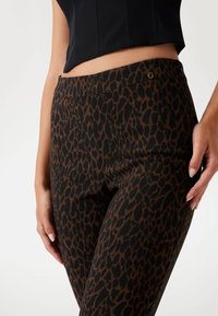 Hlače s uzorkom leoparda na crnoj pozadini i smeškastim mrljama. Imaju glatku elastičnu traku u struku i mali logo detalj blizu struka.