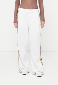 White sweatpants with wide legs, elastic waistband, and side stripes in brown and olive green. Soft texture, casual design, ankle-length.