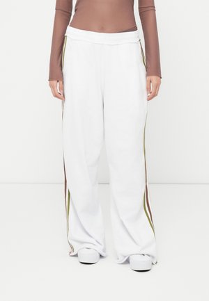 White sweatpants with wide legs, elastic waistband, and side stripes in brown and olive green. Soft texture, casual design, ankle-length.