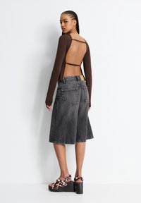 Top lungo marrone a maniche lunghe con schiena scoperta, abbinato a culottes in denim grigio. Le calzature presentano sandali con zeppa marroni con un design a macchie di mucca.