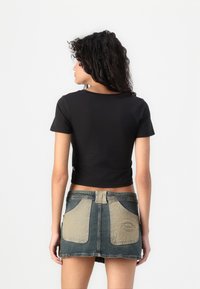 Juodas trumpas rankovėmis crop top'as derinamas su dviejų tonų džinsiniu mini sijonu, turinčiu šviesesnes priekinės kišenes ir logo pleistrą gale.