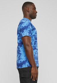 Blå tie-dye kortermet t-skjorte laget av bomull, med rund hals og avslappet passform. Ingen synlige logoer eller mønstre.