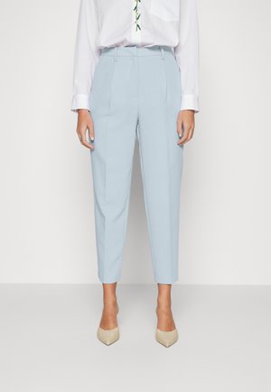 Jasnoniebieskie, dopasowane spodnie do kostek noszone z białą koszulą z długim rękawem i beżowymi butami z zaostrzonym noskiem.