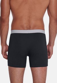 Boxer-briefs noirs avec une texture lisse et une taille gris clair. Le design présente une coupe ajustée et aucun motif visible.