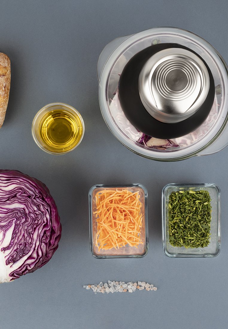 Chou rouge, conteneurs en verre de fromage râpé orange et d'herbes vertes, verre d'huile d'olive, bol et sel en roche sur une surface grise.