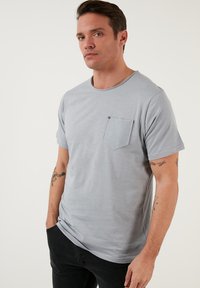 Világosszürke, rövid ujjú póló, kerek nyakkivágással, bal mellen zsebekkel, textúrált anyagból. Egyszerű dizájn, puha tapintás.