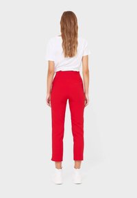 Red tailored high-waisted pants with cropped ankles, made of smooth fabric, paired with a white t-shirt and white sneakers.