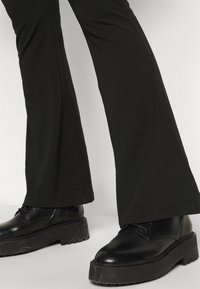 Svarta utsvängda byxor i mjukt tyg, kombinerade med kraftiga svarta läderskor med tjock sula och snörning.