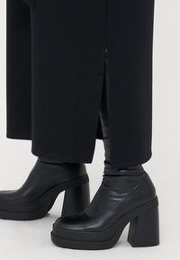 Black platform boots with a chunky heel, smooth leather texture, rounded toe, and ankle height. Leggings are also visible at the hem.