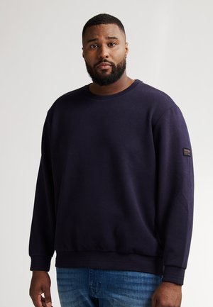 Marineblauwe sweatshirt met een gestructureerd diamantpatroon, ronde halslijn en geribde manchetten. Draag over lichtblauwe jeans.