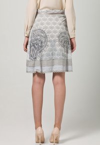 Falda en gris claro con un intrincado estampado de cachemira y borde de encaje. Cuenta con una cintura ajustada y un diseño acampanado, combinada con tacones color nude.