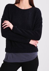 Marinblå, texturerad fleece-tröja med lös passform, rund halsringning och långa ärmar, bärs över en grå undertröja.