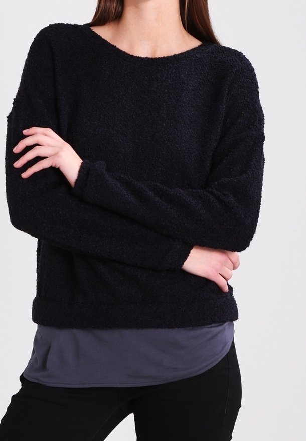 Marinblå, texturerad fleece-tröja med lös passform, rund halsringning och långa ärmar, bärs över en grå undertröja.