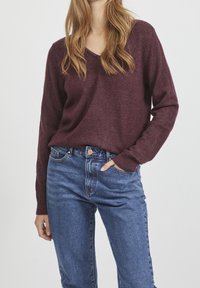 Pull col en V bordeaux en tissu doux, assorti à un jean en denim bleu taille haute. Le pull a des manches longues et des poignets côtelés.