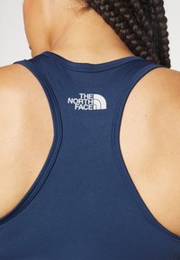 Navy blue tank top with a scoop back, featuring white The North Face logo on the upper back. Smooth fabric with athletic cut and stitching details.