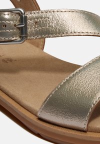 Metalliska silver sandaler med breda, texturerade remmar, spänne och en vadderad tan-fotbädd, placerade på en flexibel sula.