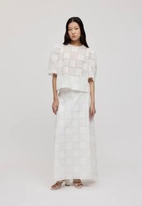Conjunto branco de duas peças com um top cropped de mangas bufantes e uma saia maxi longa, ambos com padrão recortado em grelha para adicionar textura.