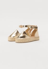 Metallic gouden espadrilles met een spitse neus, enkelbandje en gevlochten juten zool. Glad oppervlak met een glanzende afwerking.