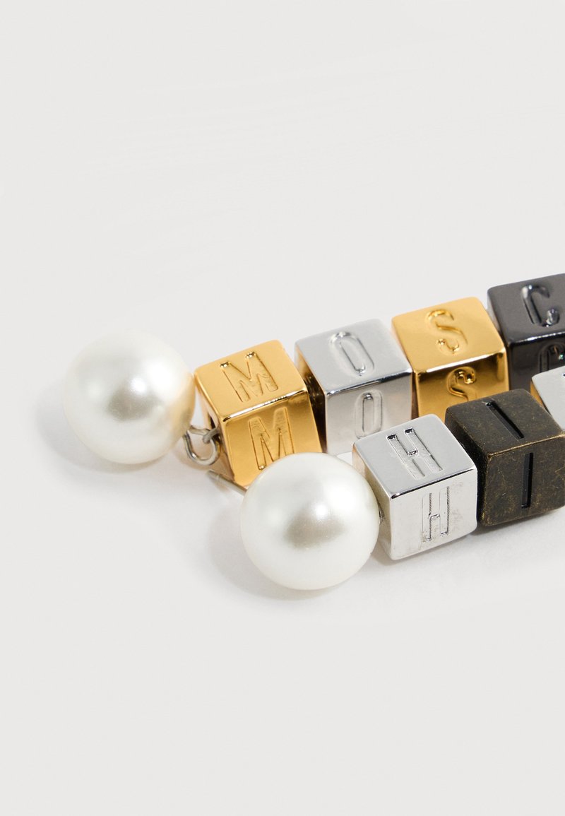 Boucles d'oreilles avec de grosses perles blanches attachées à des perles cubes en or, argent et noir, gravées de lettres formant des mots.