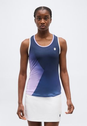 Moteris dėvi be rankovių tamsiai mėlyną ir šviesiai violetinę sportinę palaidinę su gradientu bei baltą sportinę sijoną, stovinti priešais vienspalvį foną.