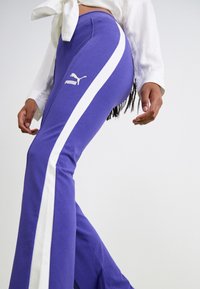 Lila utsvängda sweatpants med vita sidostreck, med en Puma-logotyp på låret, tillverkade av ett mjukt jersey-material.