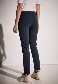 Jeans skinny azul marino con una textura suave, diseño de cinco bolsillos y cinturilla regular. Combinados con zapatillas beige.